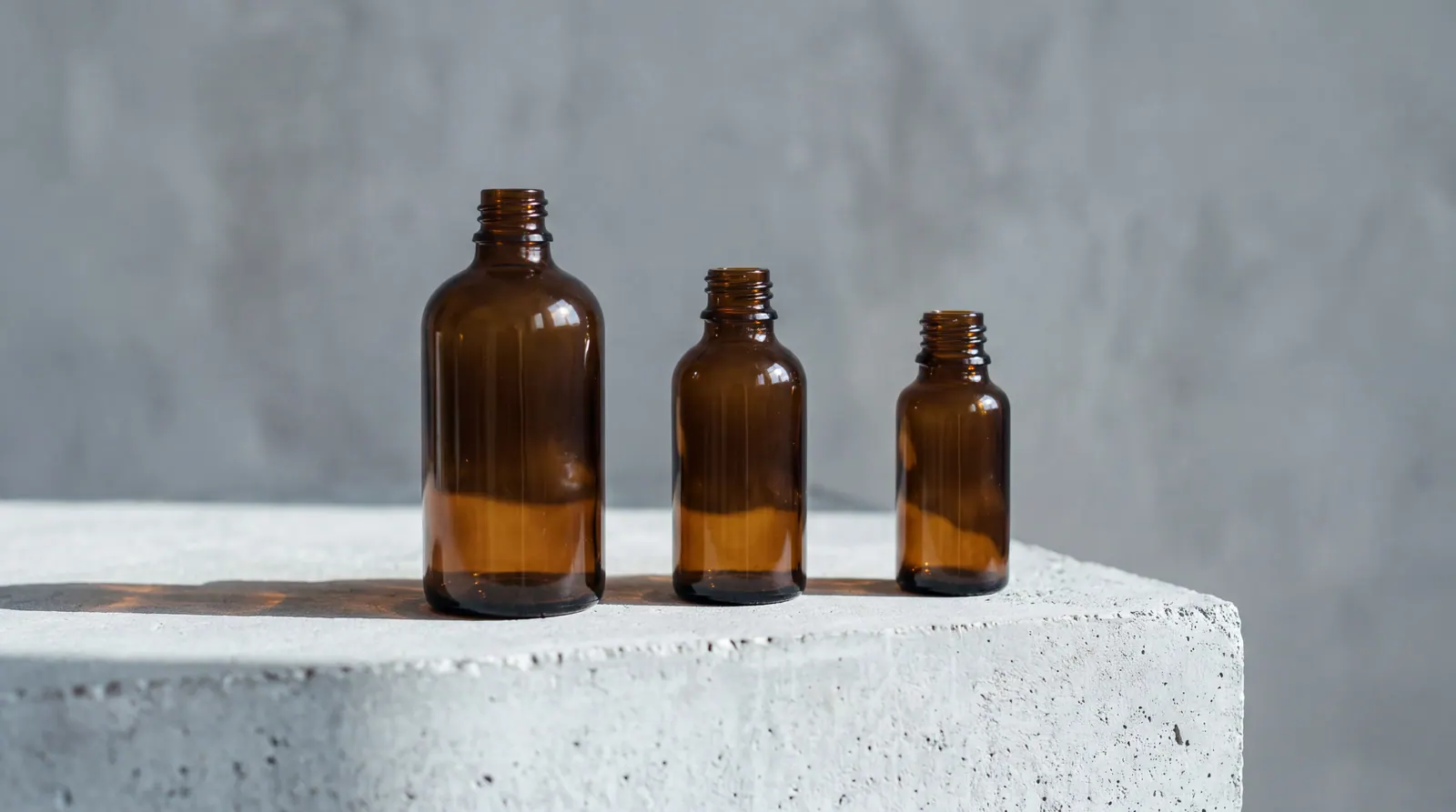 A row of amber glass supplement bottles without labels on a pale grey surface in cool directional light