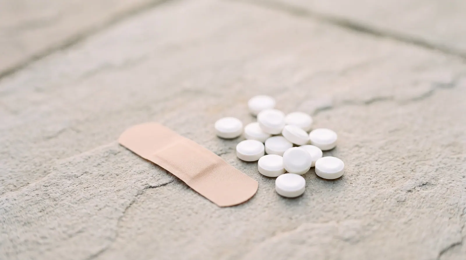 A nicotine patch and a small pile of lozenges arranged on a pale grey stone surface