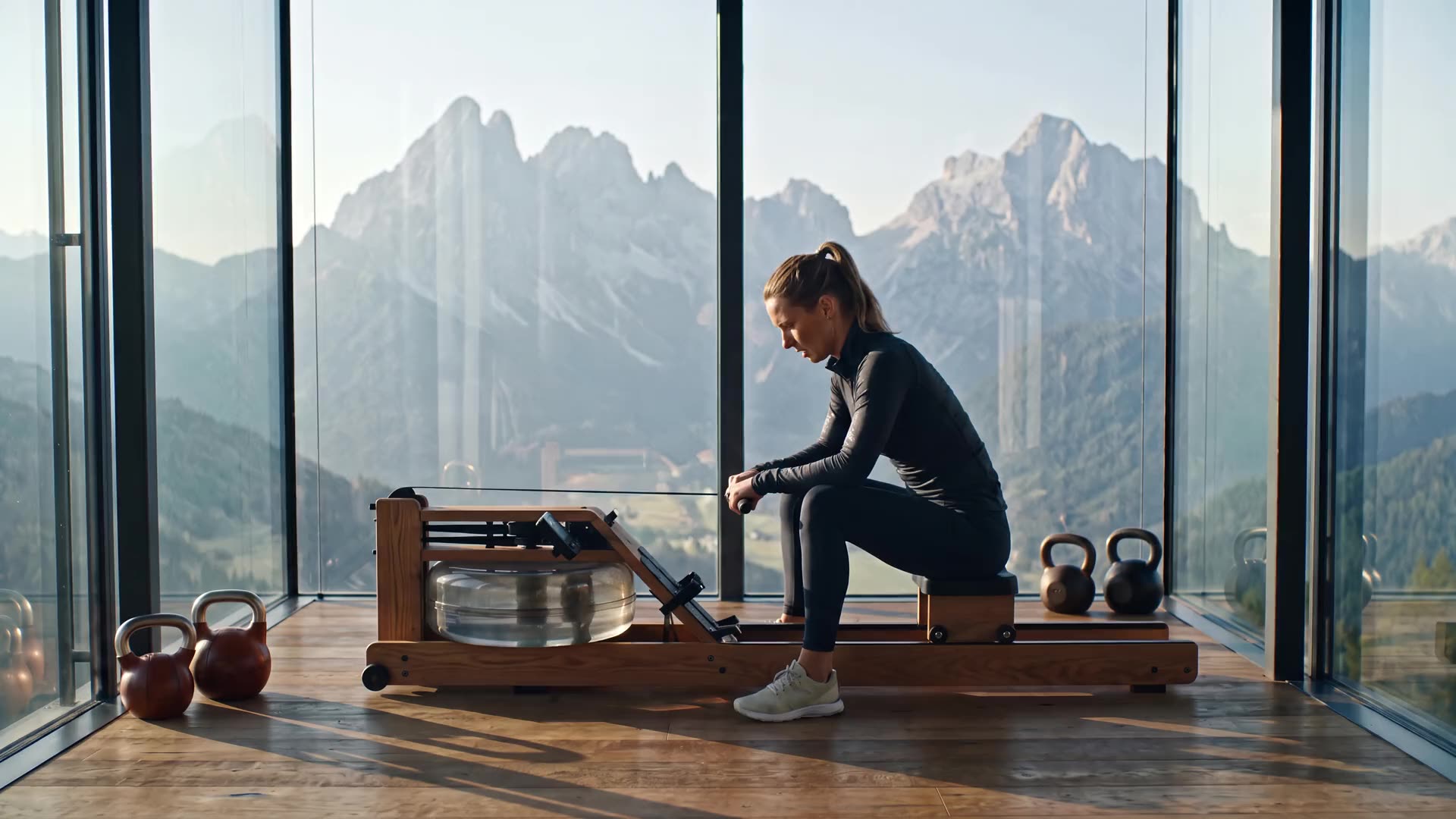 A glass-walled gym at first light with a rowing machine and kettlebells, mountain peaks filling the windows